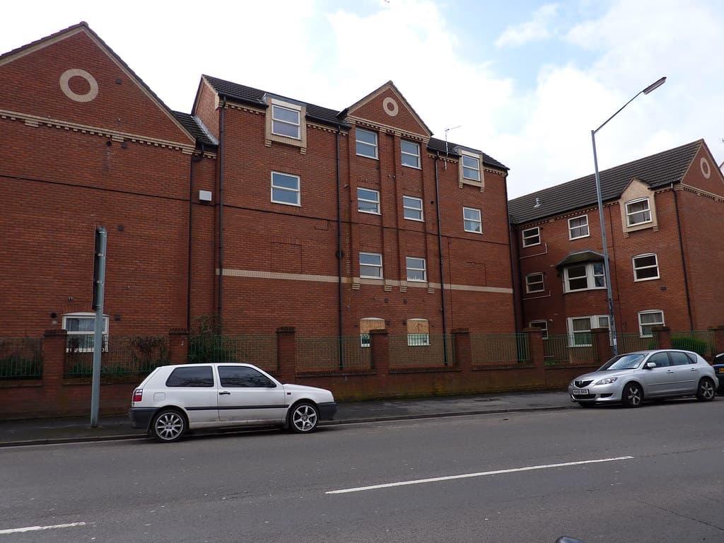 A street of modern red-brick residential apartment blocks in Leamington Spa, England, with parked cars along the kerb.
