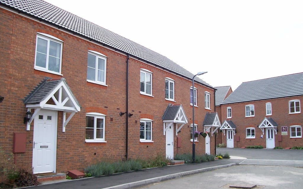 A row of modern brick terraced homes on a new residential housing estate in Warwick, England, with covered porches and a quiet street.