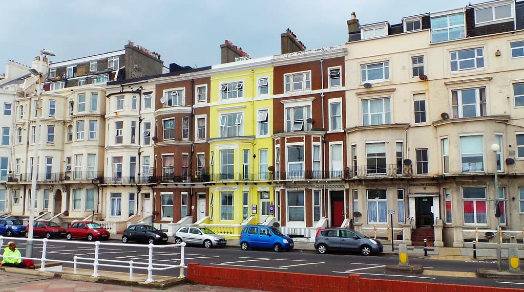 A row of multi-storey Victorian terraced houses along a seafront street in Hastings, with cars parked on the road in front.